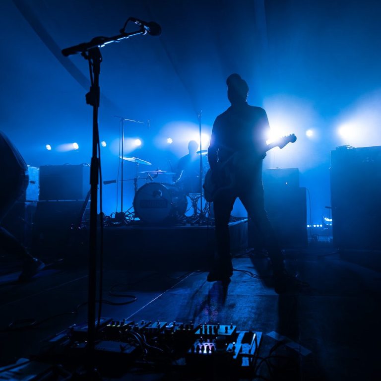 Rock band silhouette on stage with blue lights and guitar in foreground.