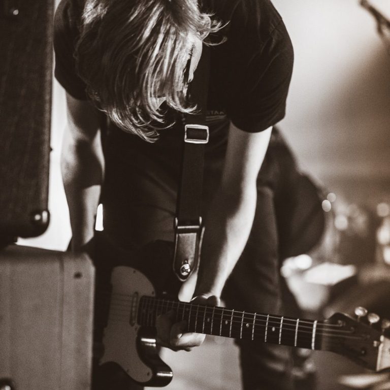 Close-up of guitarist bending over electric guitar during live show